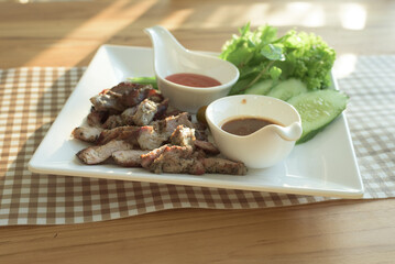 Close-up of homemade organic roasted pork served with local vegetables, chili sauce and brown sauce, in a white square shape dish on a dining table