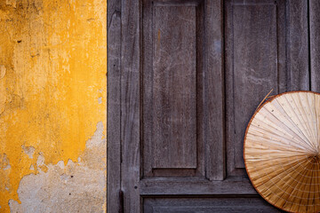 Pared amarilla antigua con puerta de madera y sombrero vietnamita. Fondo para cartelería o diseño © Javier
