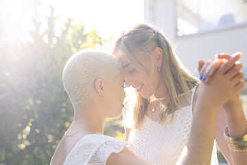 Romantic multiracial lesbian couple with face to face smiling and dancing in yard during sunny day