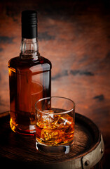Glass of whiskey with ice cubes and bottle - obrazy, fototapety, plakaty