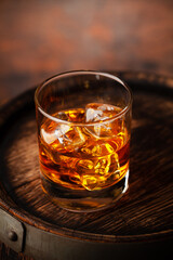 Glass of whiskey with ice cubes on the old barrel