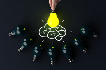 A hand holds a lit light bulb against the background of other extinguished light bulbs and a sketch...