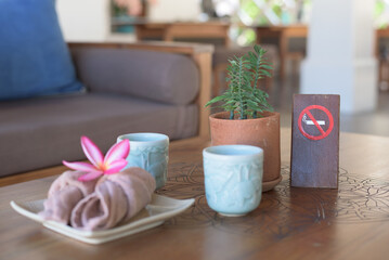Fototapeta na wymiar Selective focust on plant in clay pot near non-smoking sign. Hotel complementary set, welcome drinks and hand towels concept.