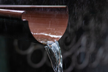 Rain water is pouring from the green draining gutter on the pavement, selective focus. - obrazy, fototapety, plakaty