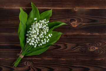 Small and fragrant spring flowers. Bouqet of lily of the valley flowers on dark wooden background