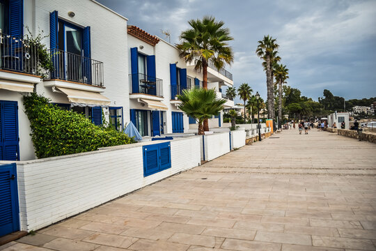 Paseo de playa con casas bajas de pescadores en blanco y azul junto a palmeras