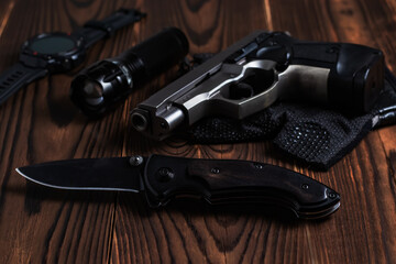Obraz premium Folding pocket knife with pistol and flashlight on wooden background