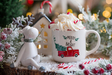 A Christmas card with cute reindeer and a mug of hot coffee on the background of a beautiful bokeh....