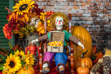 Fototapeta premium Halloween scene with doll holding box of candy corn surrounded by pumpkins and sunflowers