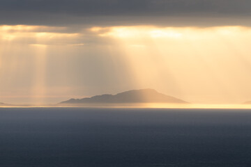 Golden rays of light shining through clouds on a heavenly evening looking towards the Outer Hebrides, seen from The Isle of Skye, Scotland, UK.