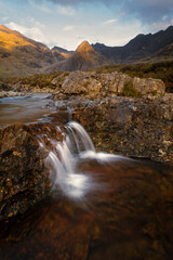 Small trickling waterfall with stunning view of Cuillin mountains dappled in golden light. Fairy Pools, Isle of Skye, Scotland, UK.