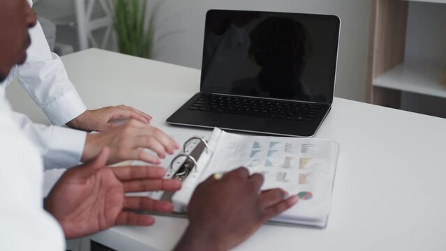 Paper report. Office worker. Data information. Unrecognizable quarreling black man checking graphics showing him by woman in light room interior.