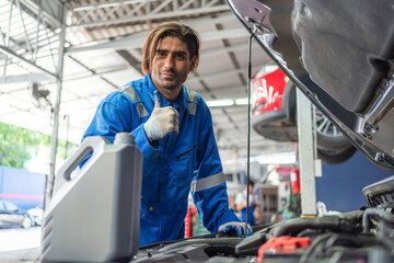 Fototapeta na wymiar Automobile mechanic repairman checking the automotive engine part in the garage. Professional vehicle maintenance man thumb up with engine bottle. Repair car service concept