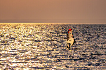 A lonely windsurfer swims towards the sun