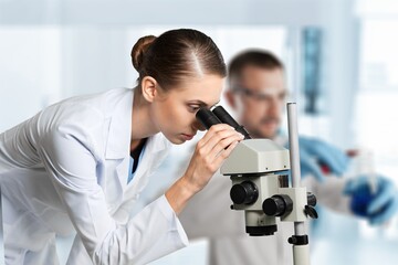 Young scientists conducting research investigations in a medical laboratory, a researcher in the foreground is using a microscope concept