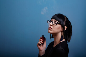 A beautiful girl with dark hair and glasses exquisitely smokes an electronic cigarette