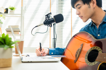 Asian young man songwriter play acoustic guitar listen song from smartphone think and write notes...