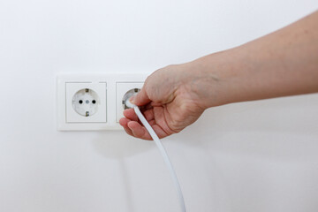 A female hand is pulling an electrical cord plugged into a socket