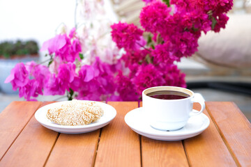 Cup of coffee and sesame cookie on the wooden table with bouquet of pink flowers
