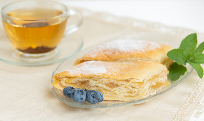 There are two slices of apple pie, blueberries and mint leaves on the plate, a cup of tea next to it