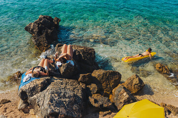 Croatian beach with people relaxing, woman on the yellow materace in the turquoise sea. Mediterranean landscape view.