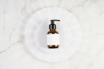 A mock-up of a brown cosmetics bottle with dispenser and white label on white round podiums on marble background, top view