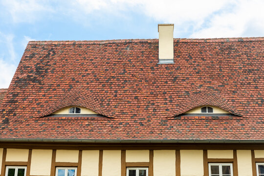 Old beautiful european german fachwerk building rooftop with eye shaped windows and chimney. Typical traditional ancoent house roof architecture in Europe. Funny face-shaped pareidolia facade
