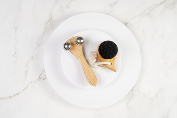 Face brush, face massage roller on white round podium on marble background, top view