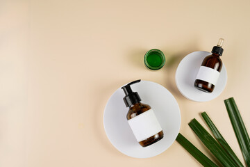 mock-up of brown cosmetics bottle with dispenser and white label, bottle with pipette on white round podium on beige colored background, green palm leaf, top view