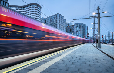 High speed train in motion on the railway station at sunset. Moving red modern intercity passenger train, railway platform, buildings, city lights. Railroad in Vienna, Austria. Railway transportation