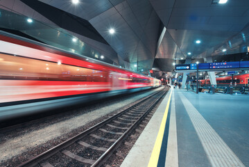 High speed train in motion on the railway station at night. Moving red modern intercity passenger...