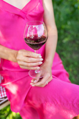Pretty young woman in a pink dress holding a glass of red wine on a summer day. Summer outdoors holiday concept.