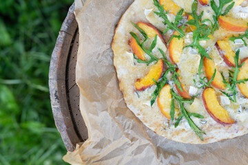 Very tasty and interesting pizza with peach and dor blue with arugula on parchment. Delicious, interesting taste of fruit pizza. Grilled pizza, outdoor recreation.