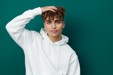 Fototapeta premium a handsome man stands on a green background in a white hoodie and poses relaxed with his hand behind his head. Horizontal Studio Photography