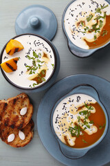 Pumpkin autumn puree soup in a pot and bowl with grilled slices, croutons and milk on a blue wooden table. Festive autumn meal