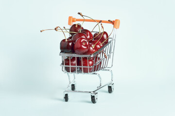 Miniature shopping cart full of ripe red cherries. Buying fruit, healthy food, vitamins.