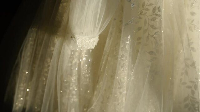 Beautiful fashion Embroidered white wedding dress is hanging on hanger in bedroom, slow motion shot, wedding day. openwork dress on a mannequin in the atelier. Close-up lacy cobweb white wedding dress