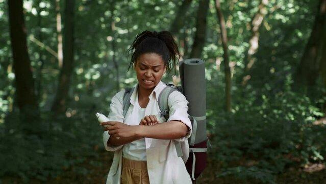 Young irritated african american woman tourist scratching hand after mosquito bite wiht repellent in forest, free space
