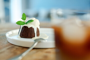 Chocolate fondant with vanilla ice cream and a glass of iced coffee on a wooden table.
