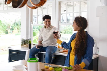 Foto op Canvas Happy biracial couple preparing food and drinking red wine in kitchen © WavebreakMediaMicro