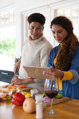 Happy biracial couple preparing food using recipe on tablet in kitchen