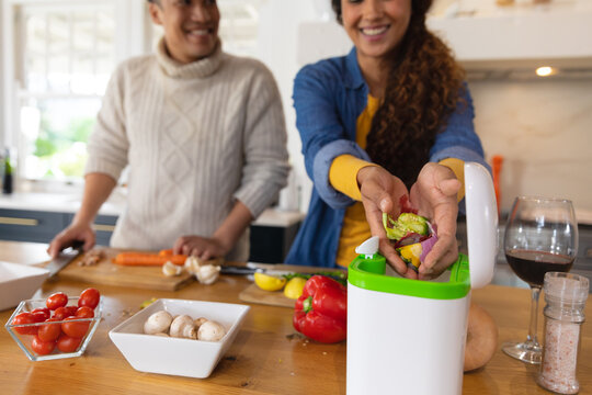 Happy biracial couple preparing food and composting vegetable waste in kitchen