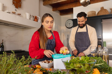 Happy caucasian couple preparing food in kitchen and composting vegetable scraps