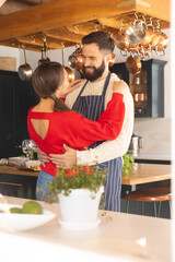 Fototapeta na wymiar Happy caucasian couple preparing food, smiling and embracing in kitchen