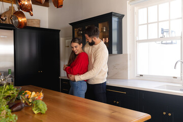 Obraz premium Happy caucasian couple smiling and embracing in kitchen