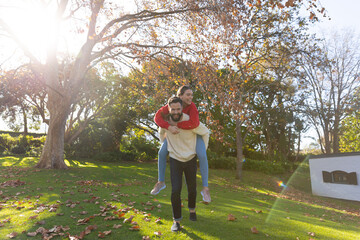 Fototapeta premium Happy caucasian couple having fun piggybacking in sunny autumn garden