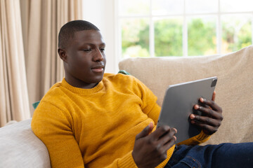Happy african american man lying on couch at home watching tablet