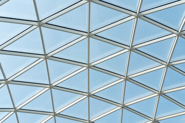 Architectural glass structure with a geometric triangular pattern on a blue sky background. Steel glass roof wall construction transparent window with support system. Transparent geometric background