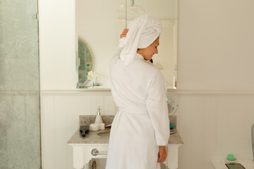 Fototapeta na wymiar Happy caucasian woman wearing robe and towel on her head in bathroom
