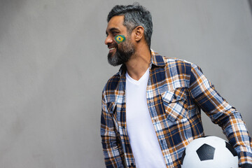 Happy biracial man with football and flag of brazil on his cheek